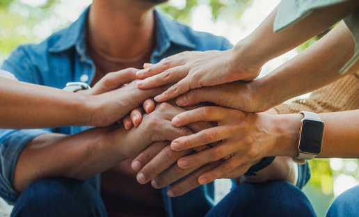 Team members place their hands together in a show of unity and teamwork outdoors.