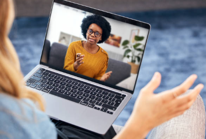 Video call on a laptop showing a Black woman in a mustard sweater speaking and gesturing.